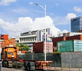 Imagem de caminhões carregados e contêineres em um porto industrial.