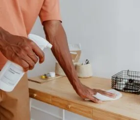 Um homem aplica spray de limpeza em uma mesa de madeira