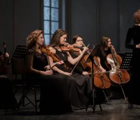 O que é música de câmara e como começar a ouvir Pequeno grupo de músicos tocando instrumentos de corda em um recital de música de câmara